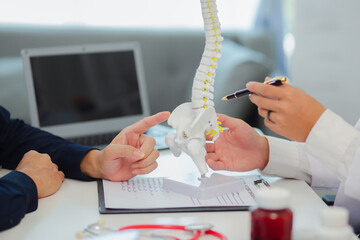 An orthopedic doctor shows a spinal model to a patient in a human spinal hospital. Diseases and...