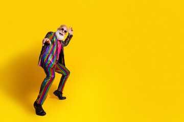 Eccentric elderly man in a vibrant striped suit posing joyfully against a bright yellow background.