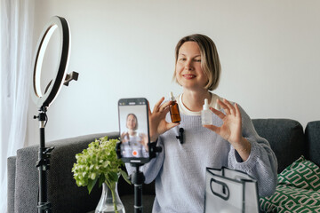 Middle-aged woman beauty blogger filming skincare product unboxing at home with ring light....