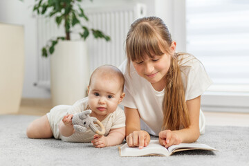 Sister reading book while baby plays nearby