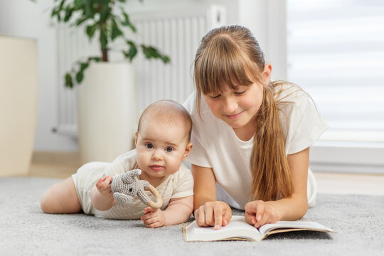 Sister reading book while baby plays nearby
