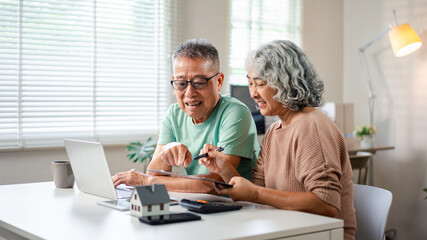 Senior Asian Couple Planning Finances at Home with Laptop and House Model for Retirement Savings and Investment for Future Real Estate