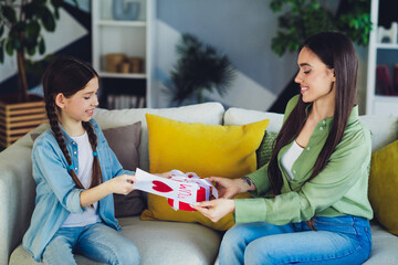 Mother and child sharing a heartfelt moment exchanging a gift with smiles on a cozy sofa at home