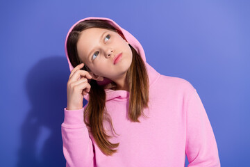 Young girl in a pink hoodie posing with a thoughtful expression against a purple background, casual...