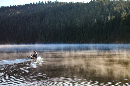 Elderly man and his dog cruising in a small fiberglass fishing boat with an electric motor on Elk River Reservoir in Idaho - Powered by Adobe