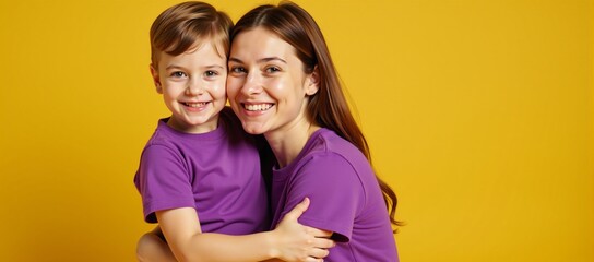 A happy mother and her smiling toddler boy pose lovingly dressed in matching violet shirts against a bright yellow backdrop celebrating their bond for Mothers Day