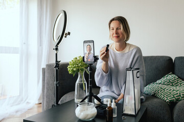 Middle-aged woman beauty blogger filming skincare product unboxing at home with ring light....