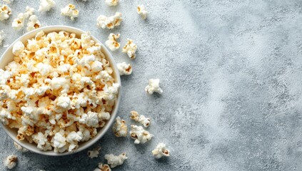 A white bowl overflowing with fluffy, lightly browned popcorn sits on a mottled grey surface; scattered popcorn pieces surround it