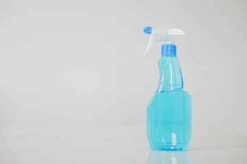 Blue glass spray bottle with white trigger in the kitchen table on a white wall background. The bottle is filled with clear blue liquid, Cleaning concept