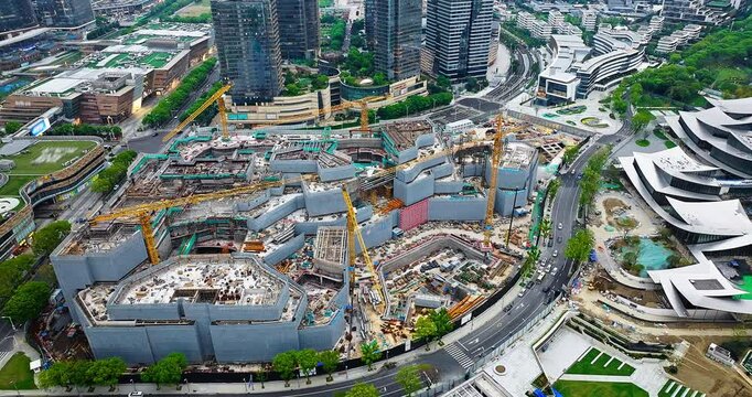 Aerial shot of a massive urban construction site with multiple tower cranes building the foundation of a modern commercial center.