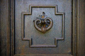 Ornate antique metal door knocker on a dark door.