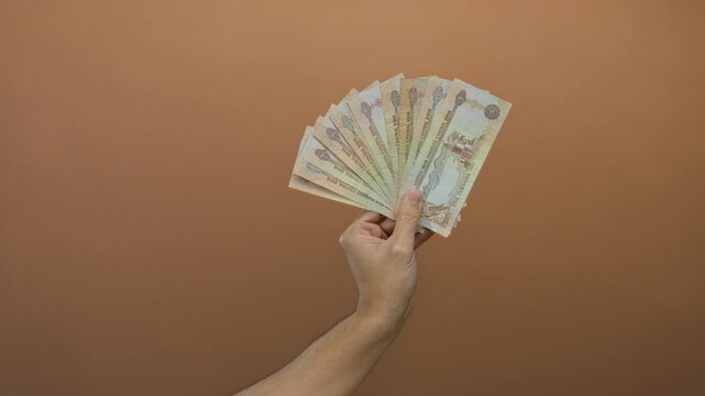 Hand holding uae dirham banknotes against a brown wall, depicting a caucasian male with an isolated money display.