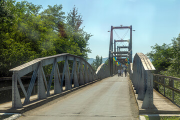 Historic Solotvyno Bridge connecting Ukraine and Romania, a symbol of cross-border connection, adorned with flags under a clear summer sky.