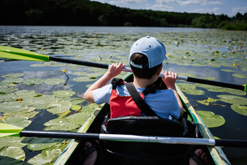 Rear view of a person paddling a canoe among lily pads on a lake