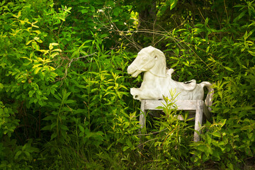 An old and abandoned rocking horse in thick foliage