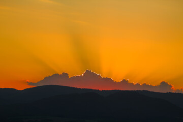 Intense golden sunset with sun rays over silhouetted hills.