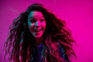 Joyful young woman with long blonde hair in glamorous blue dress against neon pink background
