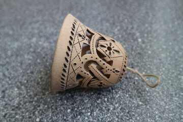 There is a beige bell on the table. There is a bell with a carved pattern. Openwork ceramic bell