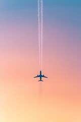 Airplane silhouette flying into sunset with contrails in the sky