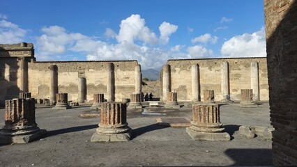 Pompeii, Italy - 8 January 2025. The basilica ruins feature stone column stumps and fluted pillars against ancient walls, with Mount Vesuvius visible in the background. © Michael