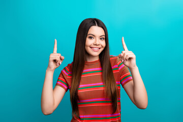 Young woman pointing up with her hands and smiling brightly against a vibrant turquoise background...