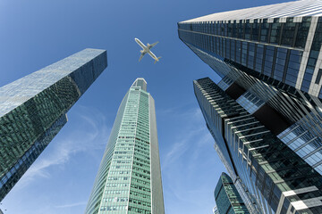Modern glass skyscrapers on a clear day and passenger aircraft flying over them