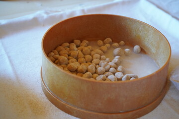 A round wooden sieve contains small, round dough balls, the 