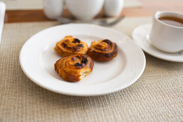 Three raisin pastries served on white plate during hotel breakfast. Morning dessert, sweet bakery snack, and elegant table setting concept.