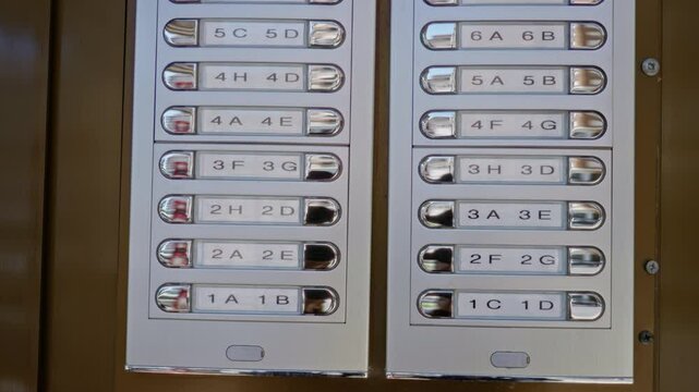 Metallic apartment intercom panels with sunlight reflecting outdoors, displaying numbered buttons against a sunny background environment.