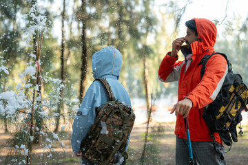 Fototapeta premium Adventurous Couple Exploring Snowy Forest Trail – Man Pointing While Woman Stands Beside with Trekking Poles, Both Dressed in Winter Hiking Gear under Gentle Snowfall in Nature