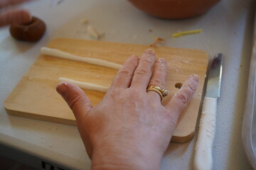 A woman's hand with flour on it rests on a wooden cutting board with two thin strips of dough. A...