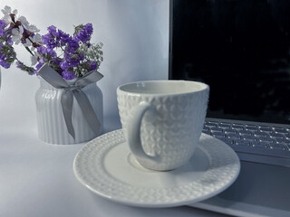 Elegant still life composition with a textured white ceramic cup and saucer placed next to a laptop...