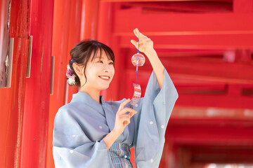 Japanese woman in yukata holding a wind chime in front of the red torii gate of the shrine
