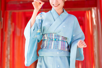 Japanese woman in yukata holding a wind chime in front of the red torii gate of the shrine