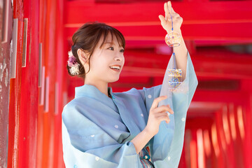 Japanese woman in yukata holding a wind chime in front of the red torii gate of the shrine