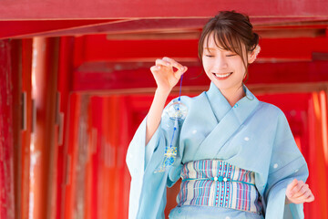 Japanese woman in yukata holding a wind chime in front of the red torii gate of the shrine