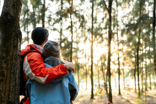 Couple Hugging in Forest at Sunset. Rear View of Romantic Travelers in Warm Winter Clothes Standing Together, Embracing Peacefully While Enjoying the Tranquil Nature and Soft Golden Light - Powered by Adobe