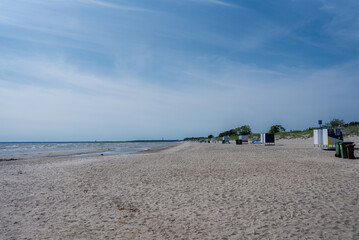 A tranquil sandy beach in Parnu, Estonia, with small structures near grassy dunes, a calm shoreline, and a faint horizon where sea meets sky.