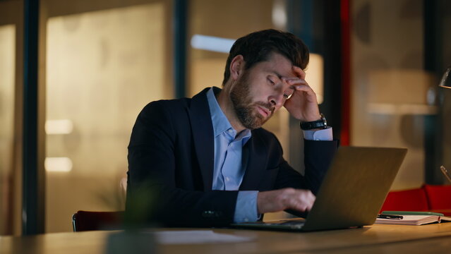 Overworked businessman typing laptop checking time at night office closeup.
