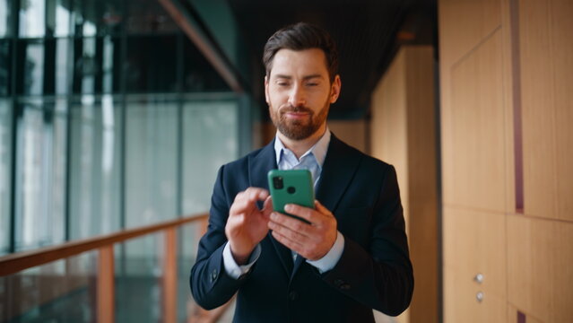 Smiling entrepreneur reading smartphone message walking modern hallway closeup