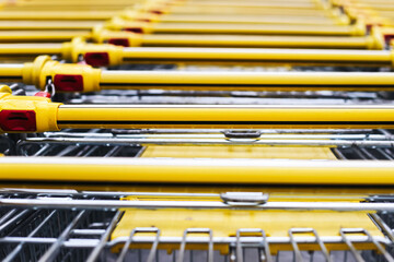 Yellow shopping carts. Row of trolleys outside. Commercial retail scene. Abstract industrial pattern. Supermarket detail view.