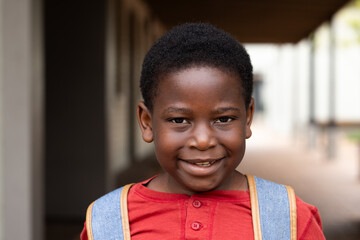 Smiling african american boy with backpack standing in school hallway, ready for class