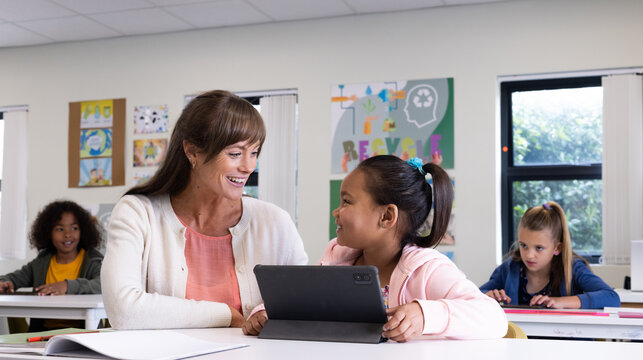 Female teacher and girl using tablet in classroom, smiling and engaging in learning