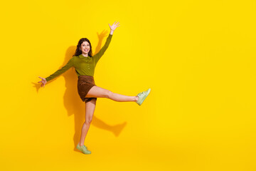 Young cheerful woman dressed stylishly in trendy khaki and green clothing dancing against vibrant...