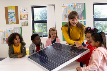 Explaining solar panel, female teacher engaging diverse children in classroom, at school