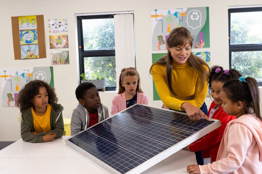 Explaining solar panel, female teacher engaging diverse children in classroom, at school - Powered by Adobe