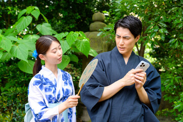 Obraz premium 浴衣姿の女性がスマートフォンを操作する男性をのぞき込もうとするも男性が不快感を示す夏の一場面