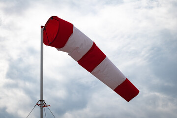 A windsock on a metal pole against a cloudy sky indicates a wind blowing from the left at about 3-6...