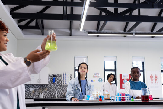 In school, female teacher demonstrating chemistry experiment to diverse students in classroom