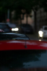On a lively urban street at night, a bright red car is parked under glowing street lights, while...
